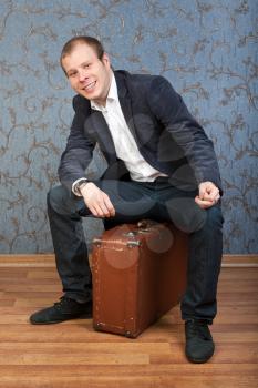 casual man sitting on an old brown retro suitcase