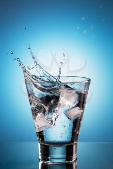 Ice cube splashing into a glassl of water. Blue background