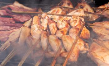 fried chicken on skewers over charcoal in a smoke in Thailand