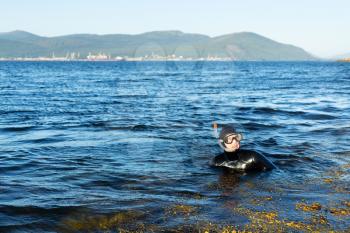 underwater hunter in a wetsuit in the water on the background of the port with cranes in the background