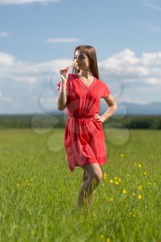 20 year-old girl in red dress sniffing a yellow flower in a field on a sunny day