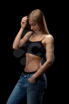 Beautiful 20-year-old girl in jeans in the top bare belly in the studio. Isolate on a black background.