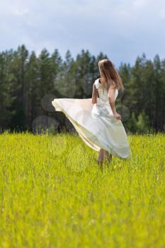 woman in a wedding dress swirls in the field, view from the back