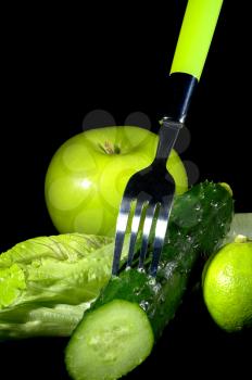 group of green vegetables and fruits with fork over black background