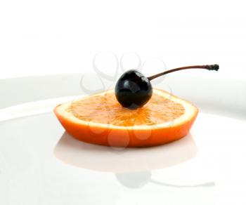 slice of orange with cherry on top isolated on a plate with reflection