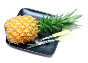 ripe vivid pineapple on a black plate with knife and fork isolated over white