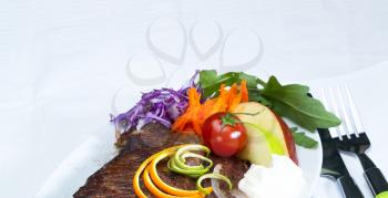 fresh juicy beef ribeye steak grilled with lemon and orange peel on top and vegetables beside with sour cream
