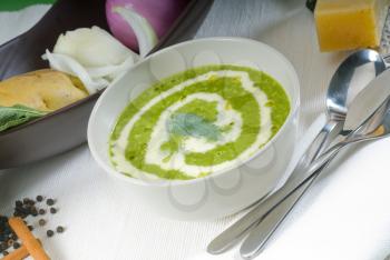 fresh spinach soup on a white bowl with sage and cream on top