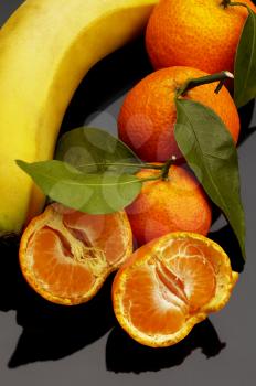 vivid orange tangerine and banana on black reflective surface