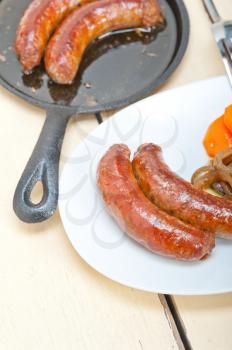 beef sausages cooked on iron skillet with carrot and onion