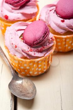 fresh pink berry cream cupcake with macaroon on top over rustic wood table