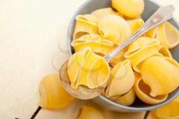 raw Italian snail lumaconi pasta on a blue bowl over rustic table macro