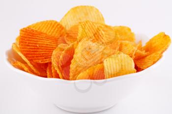Potato chips in white bowl isolated on gray background.