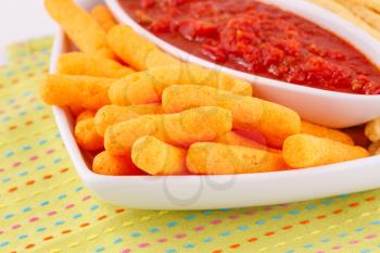 Corn chips and red sauce on colorful tablecloth.
