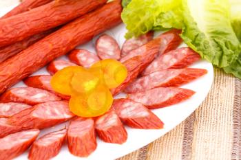 Fresh sausages in plate and green salad leaves on bamboo mat background.