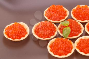 Red caviar in round pastries on brown plate.