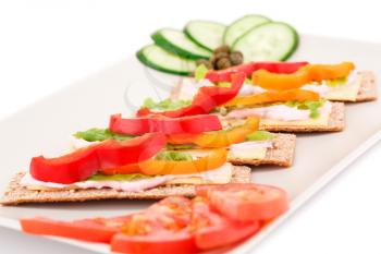 Crackers with fresh vegetables and cheese on beige plate.
