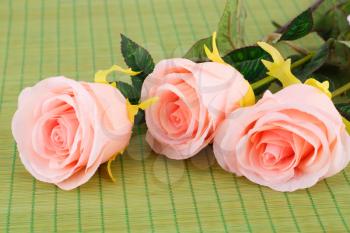 Pink fabric roses on bamboo background, closeup picture.