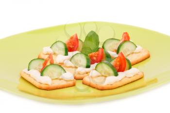 Crackers with fresh vegetables and cream on green plate.