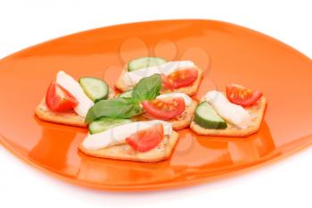 Crackers with fresh vegetables and cream on orange plate. 