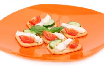 Crackers with fresh vegetables and cream on orange plate.