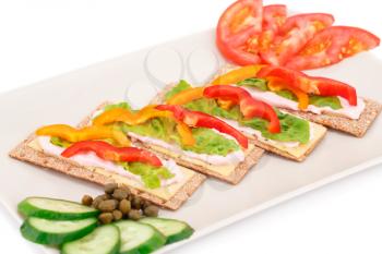 Crackers with fresh vegetables and cheese on beige plate.