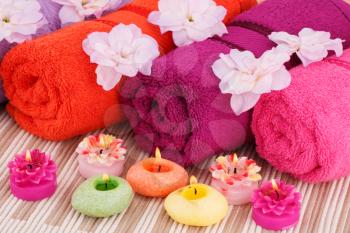 Spa set with towels, candles and flowers on fabric background.