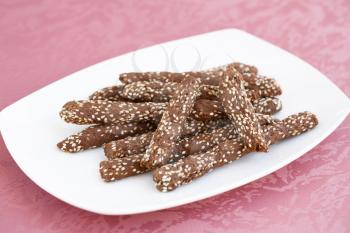 Carob crackers with sesame seeds  in white plate on pink cloth background.