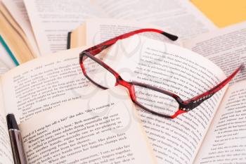 Opened books, eyeglasses and pen close up picture.