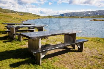 Landscape with mountains, lake, wooden benches, sky and clouds in Norway.