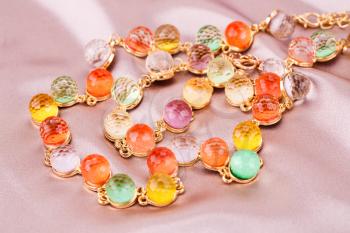 Necklace and bracelet with colorful stones on pink silk background.