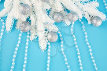 Christmas decoration with gray balls, beads and fir-tree white branch on the blue background.