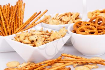 Different salted crackers in bowls on white background.