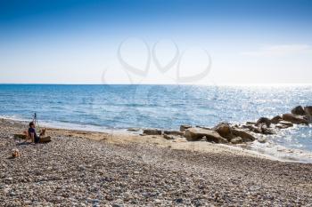 Blue Mediterranean sea with the sparkling surface, stones and the man with dogs on beach in Cyprus.