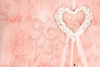 White wooden heart with ribbon on pink fur background.