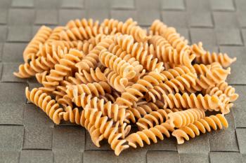 The heap of fusilli pasta on the gray bamboo place mat.