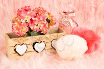 Beige wooden box, flowers, bottle and fluffy pompons on pink fur background.