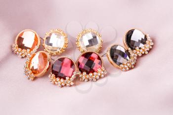Stylish earrings with stones on fabric background.