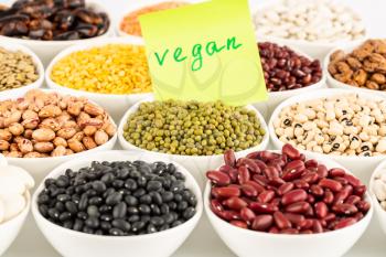 The collection of different beans and peas in the ceramic bowls with notice vegan.