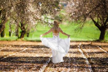 Young beautiful romantic blonde woman in white dress in blooming garden.