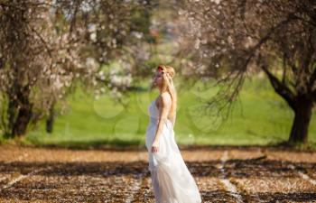 Young beautiful romantic blonde woman in white dress in blooming garden.