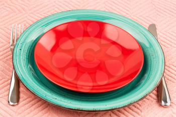 Two colorful empty plates with knife and fork on pink cotton towel.