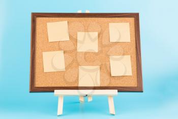 Wooden easel with cork boardand paper stickers on blue background.