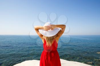 Blond woman in the red dress with the white hat at the beach in Cyprus.