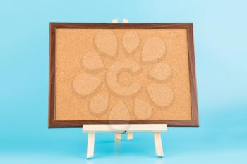 Wooden easel with cork board on blue background.