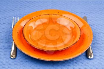 Two orange empty plates with knife and fork on blue cotton towel.
