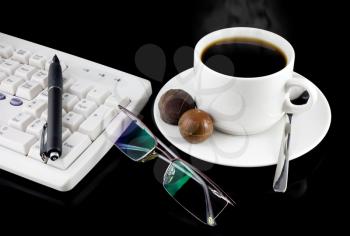 Cup of coffee, part of keyboard,mouse on a black background.