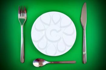 Table serving-knife,plate,fork on  green colour background.