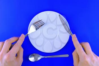 Table serving-knife, fork in hands on blue background.