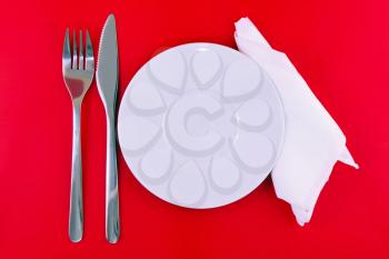 Table serving-knife,plate,fork and silk napkin  on  red colour background.
